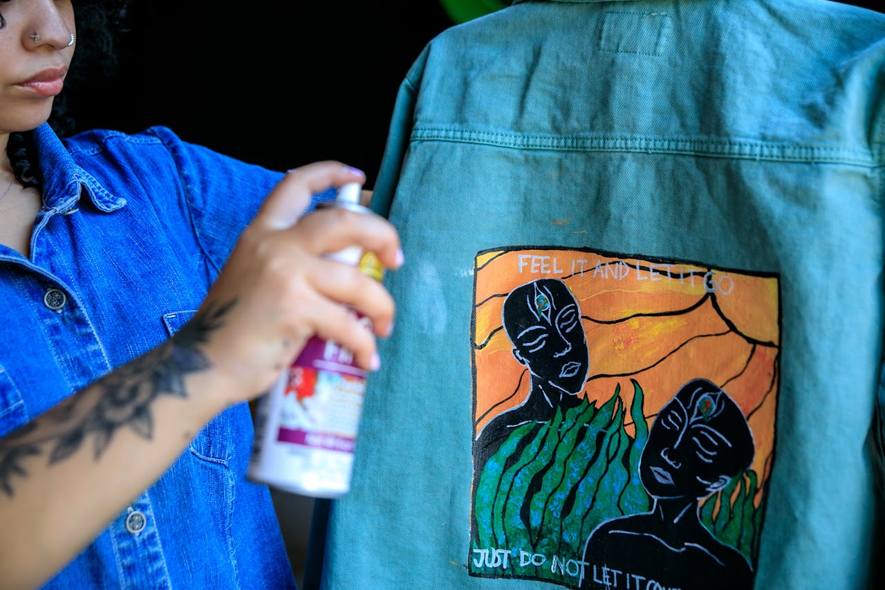Woman artist spray painting a denim jacket with unique artwork design.